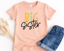 Load image into Gallery viewer, A pink t-shirt with the text "BIG SISTER" printed on it, along with a pair of blue jeans.
