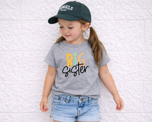 Load image into Gallery viewer, A young girl wearing a green baseball cap and a gray t-shirt with the text "Big Sister" is leaning against a white wall.
