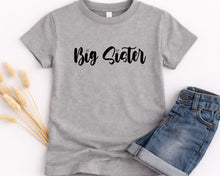 Load image into Gallery viewer, A gray t-shirt with the text "Big Sister" printed on it, along with a pair of blue jeans, are displayed on a white background.
