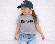 Load image into Gallery viewer, A young girl wearing a grey t-shirt with the text "Big Sister" and a green baseball cap stands against a white wall.
