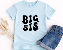 Load image into Gallery viewer, A light blue t-shirt with the text "BIG SIS" printed on it, along with a pair of denim shorts.
