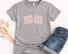 Load image into Gallery viewer, A gray t-shirt with the text "BIG SIS" printed on it, along with a pair of blue denim shorts, are displayed on a white background.
