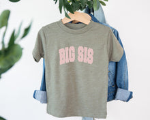 Load image into Gallery viewer, A gray t-shirt with the text "BIG SIS" printed on it, hanging on a wooden hanger.
