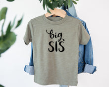Load image into Gallery viewer, A gray t-shirt with the text "big SIS" printed on it, hanging on a wooden hanger.
