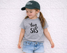 Load image into Gallery viewer, A young girl wearing a green baseball cap and a gray t-shirt with the text "big SIS" is leaning against a white wall.
